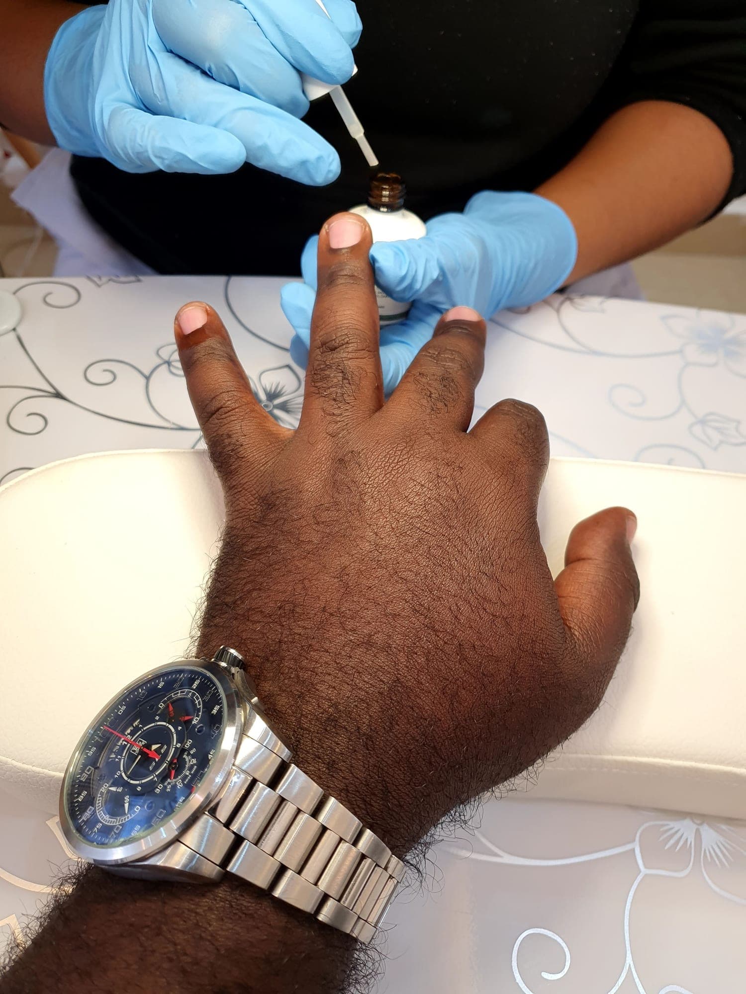 A nail technician in blue gloves painting a client’s nails at the spa.